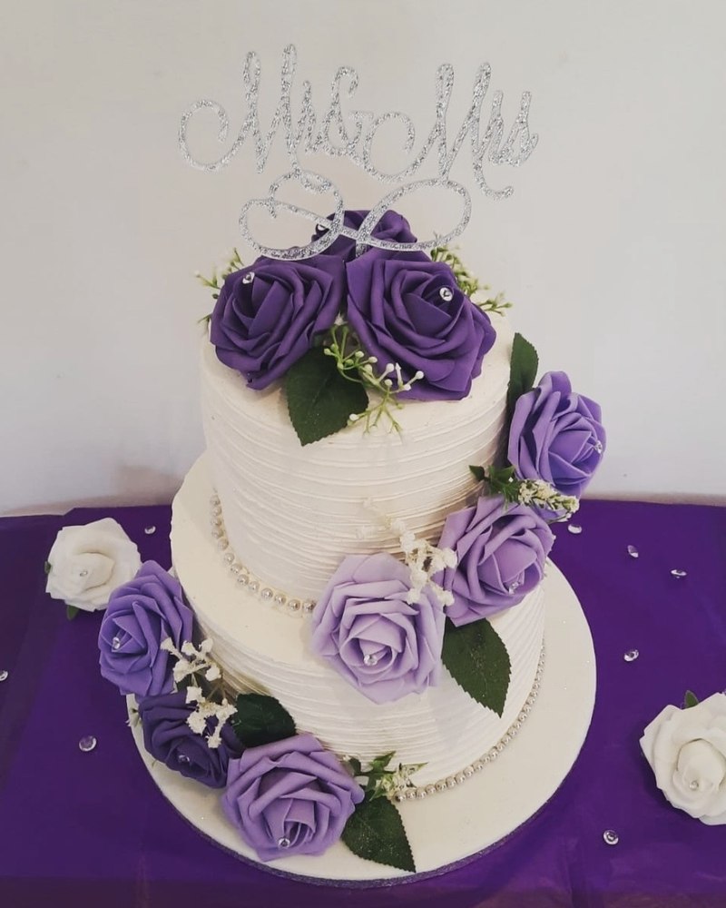 Two-tier ivory wedding cake with purple and lilac roses and Mr & Mrs topper
